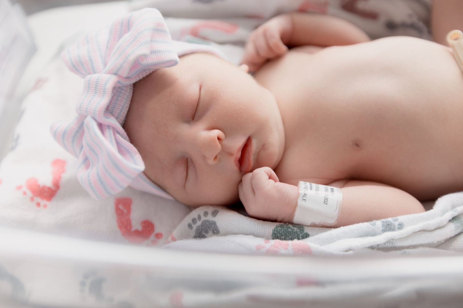 Sleeping newborn resting on white blanket with subtle pink and gray animal prints.