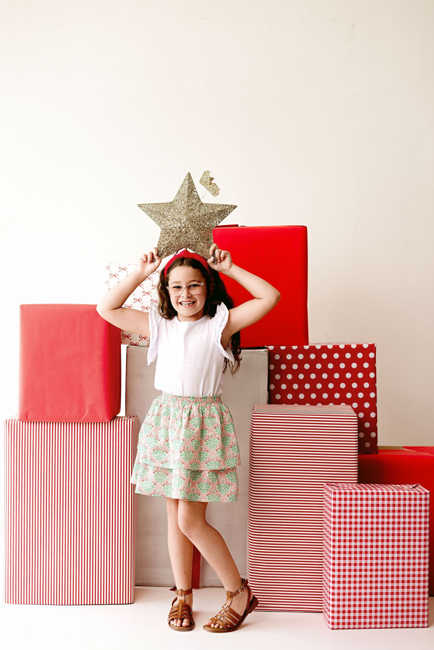 A series of four progressive photos showing a child posing playfully with red and white patterned gift boxes.