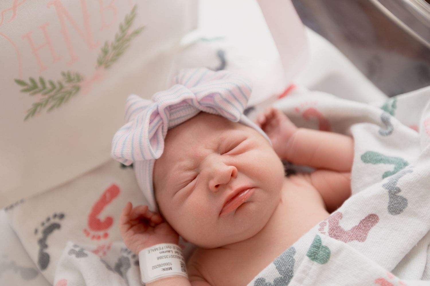 Close up of newborn with pink bow headband lying on dinosaur patterned blanket during first photo session.