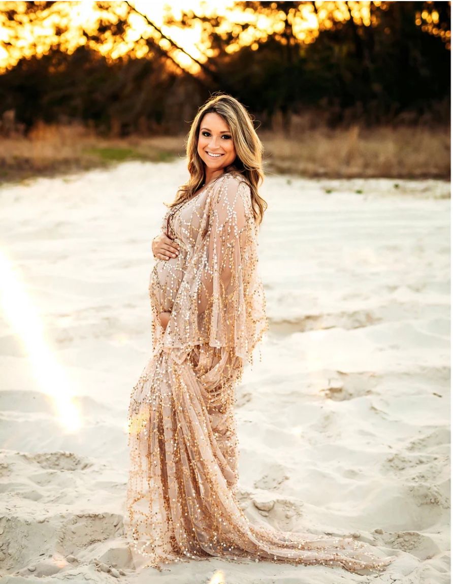 A person in a sequined champagne-colored gown poses on a sandy beach at sunset with golden light in the background.