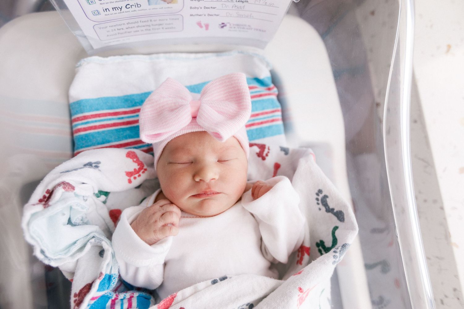 Newborn baby sleeps peacefully in hospital bassinet wearing pink bow and striped hospital blanket during Fresh 48 session in Beaumont.
