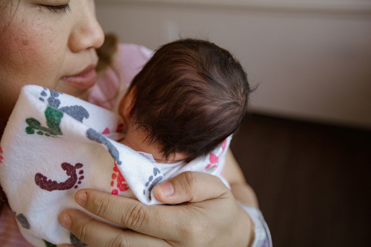 A newborn baby wrapped in a printed blanket with footprints and birds.
