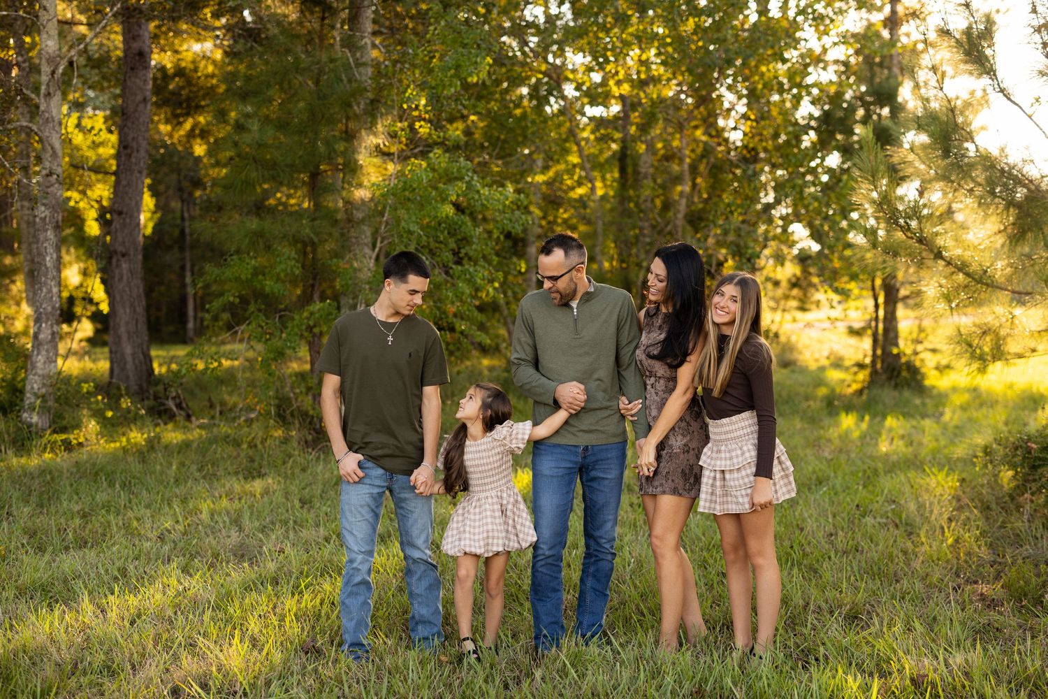 A group of people stand together in a sunlit meadow during golden hour while wearing casual clothing.