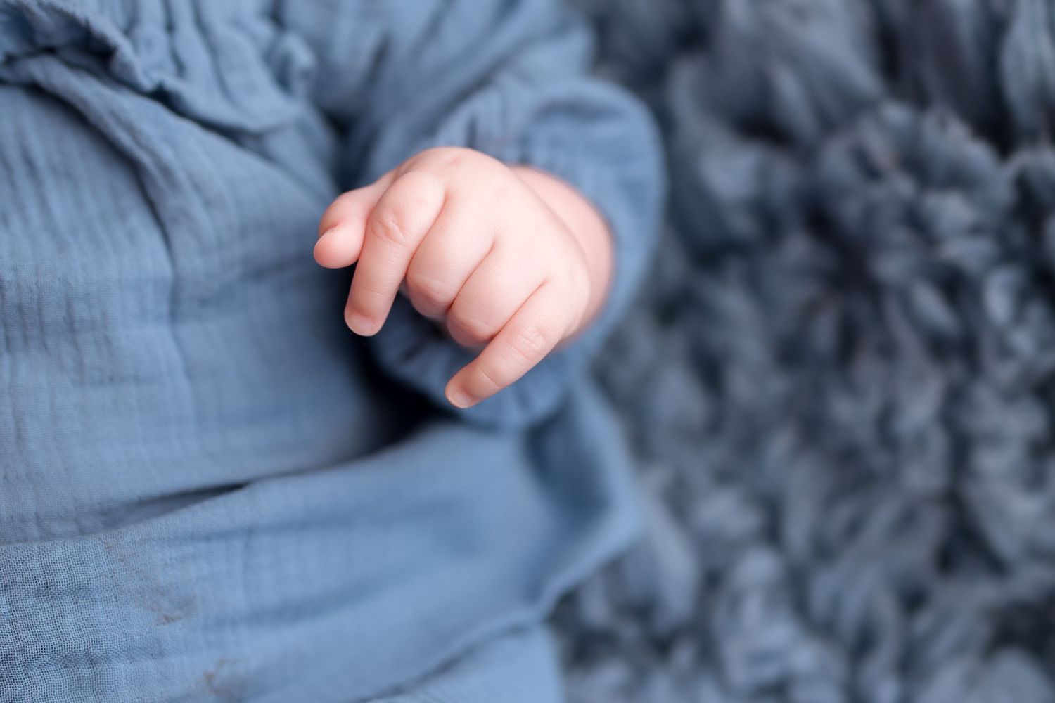 A close-up photo of a newborn baby's tiny hand grasping an adult's finger against a soft blue background.