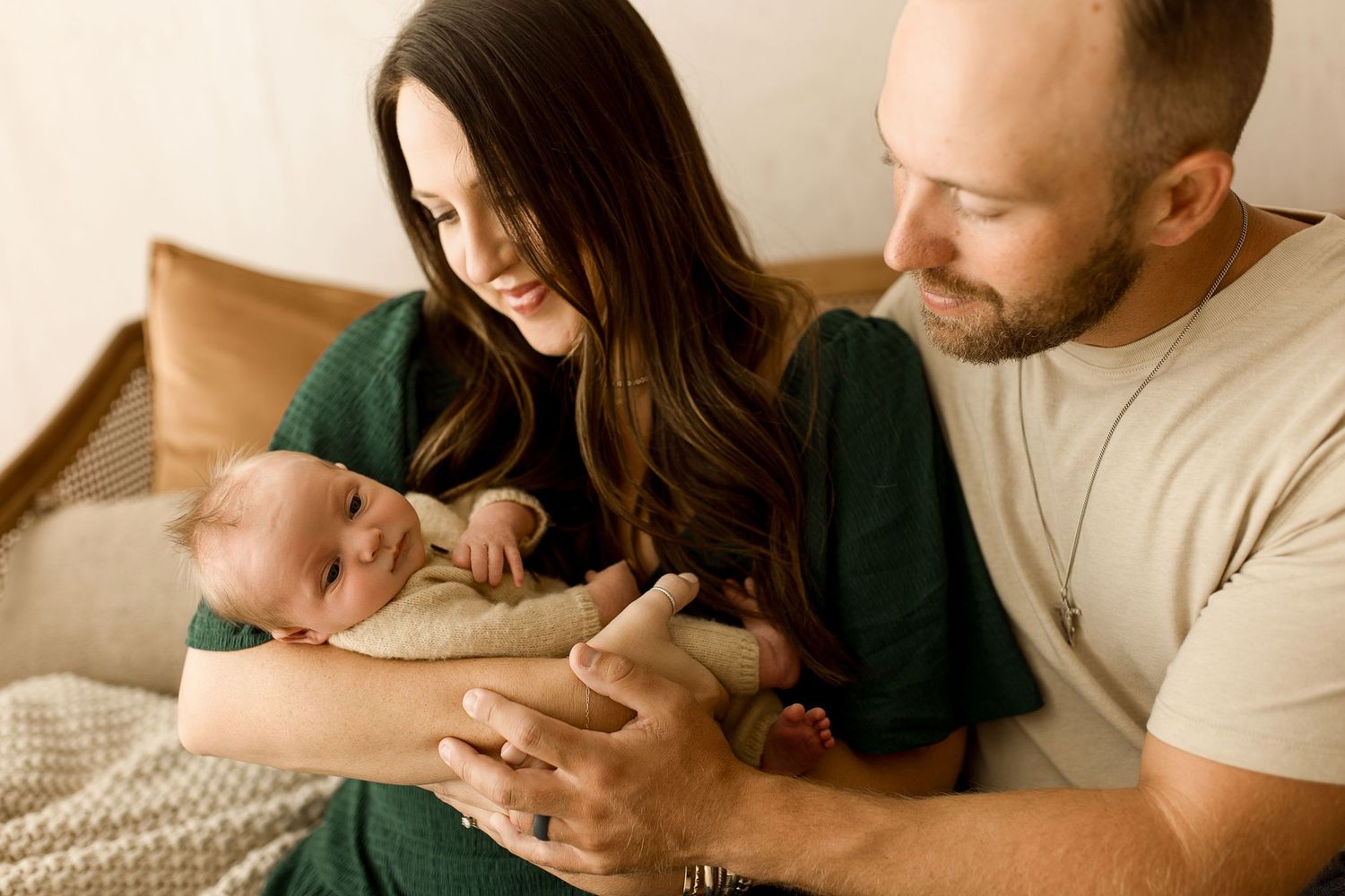 Parents lovingly hold their newborn baby while sitting together on a couch with a cozy knit blanket.