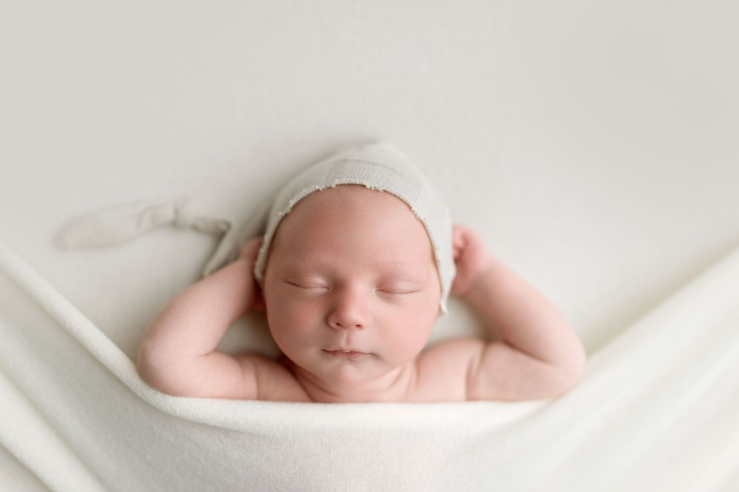 A sleeping newborn baby swaddled in soft white fabric rests peacefully against a light background.