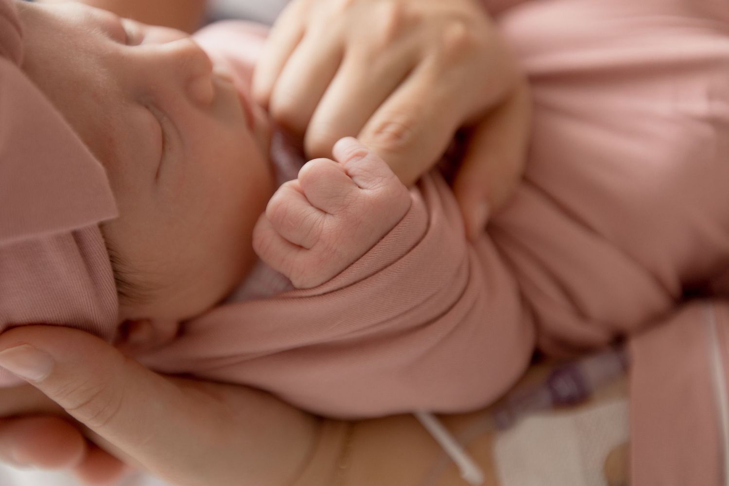 Close-up view of tiny baby fingers grasping gently in soft pink lighting.