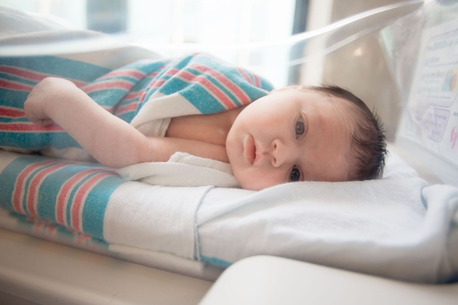 Newborn baby resting in striped hospital blanket near window during Fresh 48 session in Beaumont hospital.