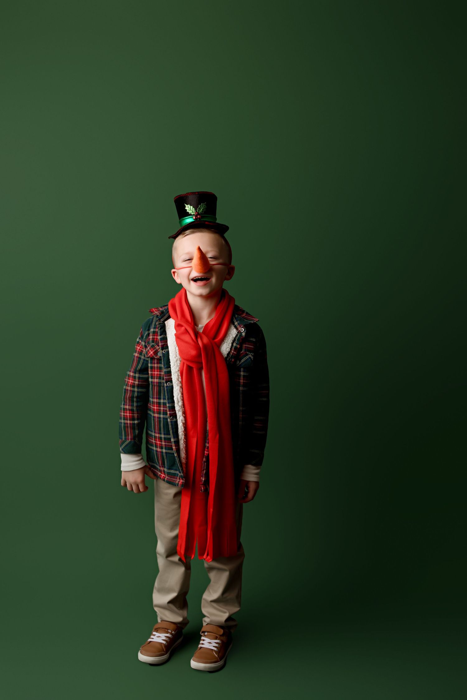 Child wearing plaid jacket, red scarf and top hat poses against green background.