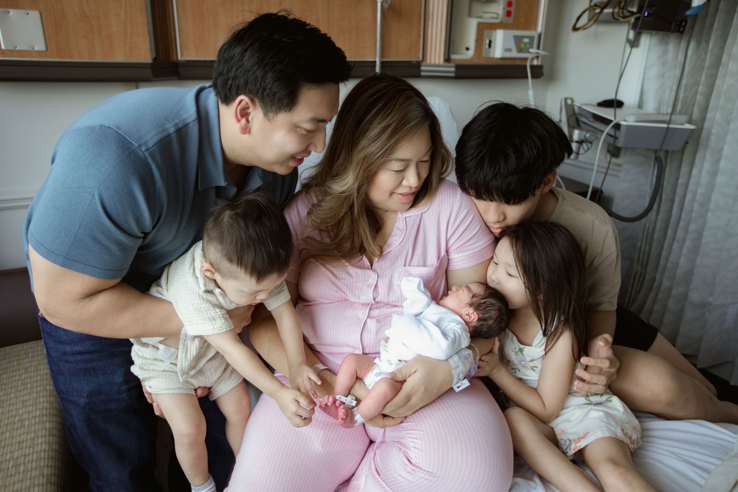A newborn baby surrounded by family members in a hospital room setting.