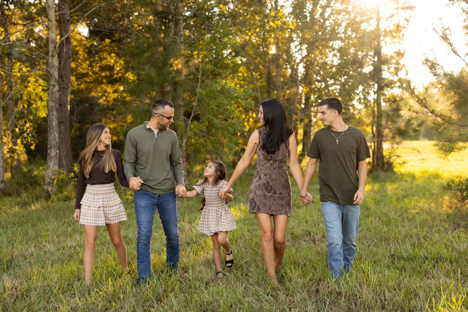 A group walks together through a sunlit meadow at golden hour, holding hands in a line.