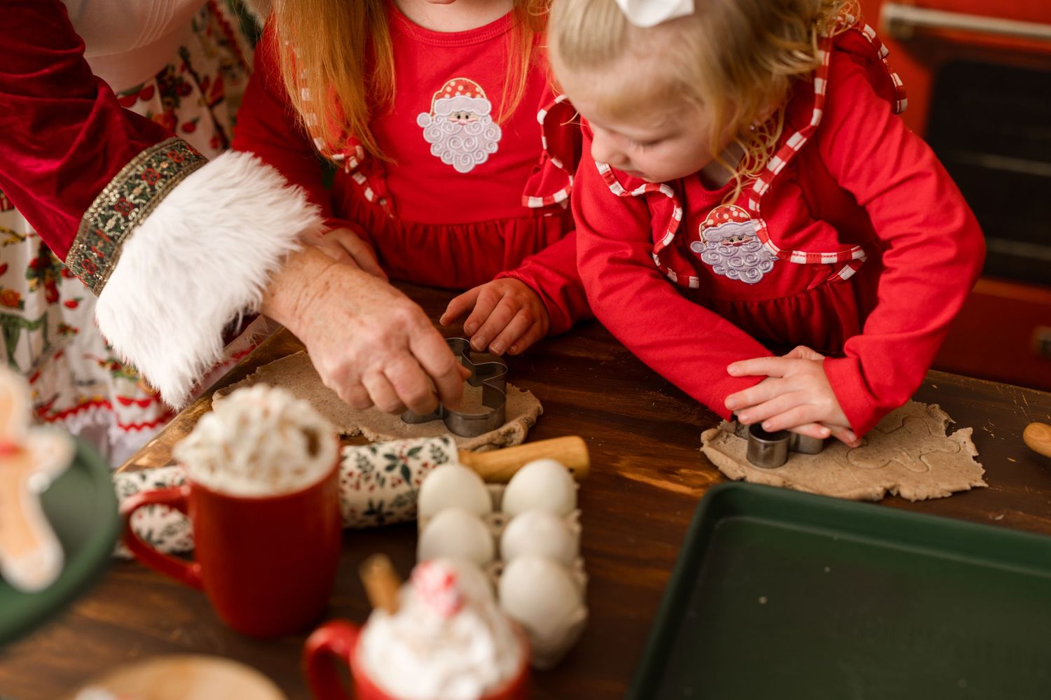 Children in matching red sweaters decorate Christmas cookies with white frosting and sprinkles at a wooden table.