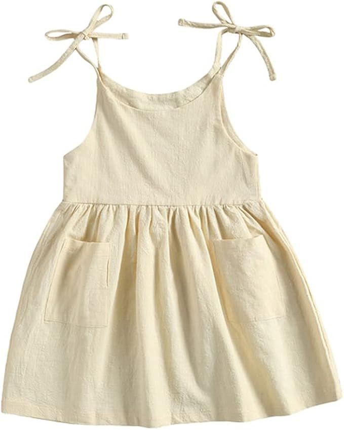 Beige linen toddler dress with tie shoulder straps and front pockets features a gathered waistline and A-line silhouette.