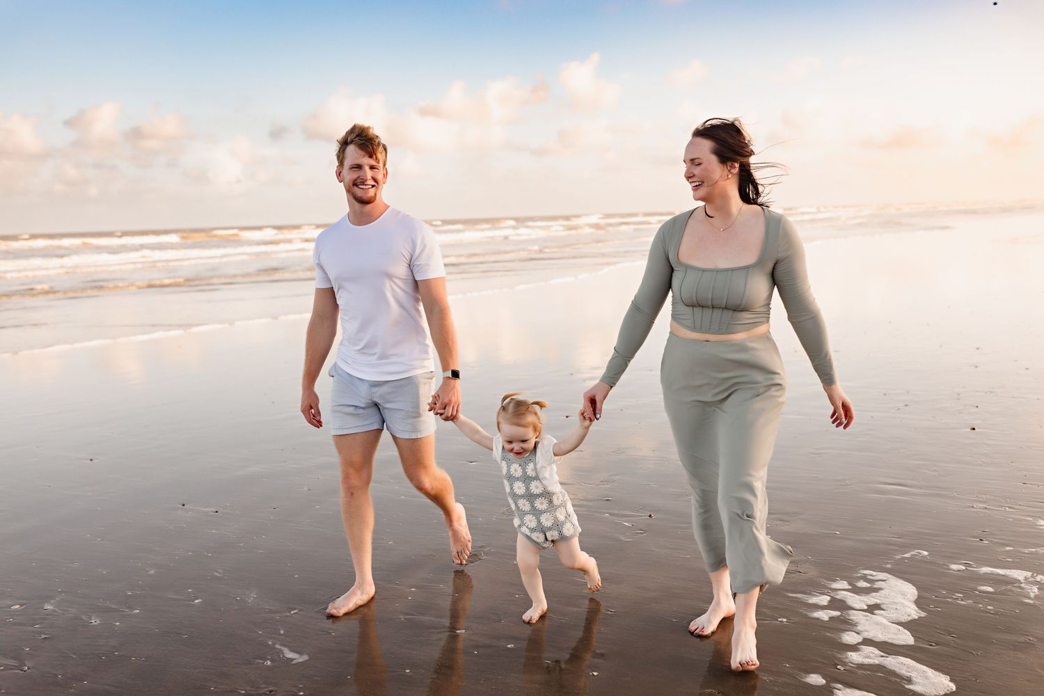 A family walks hand in hand along the shoreline during sunset at the beach.