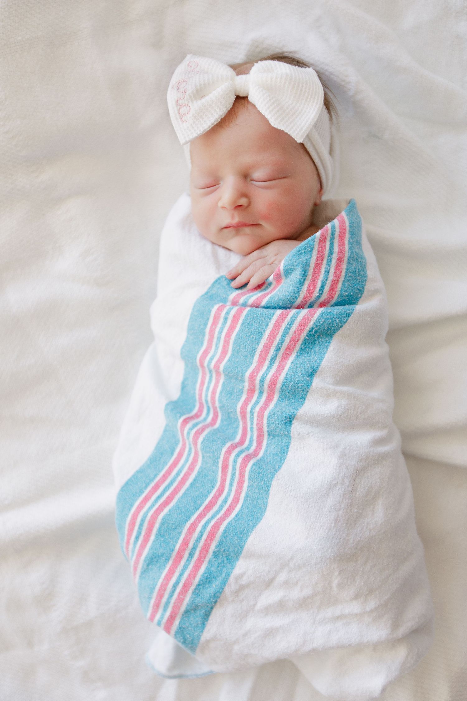 Newborn wrapped in white blanket with blue and pink stripes sleeping peacefully during Fresh 48 session in Beaumont hospital.