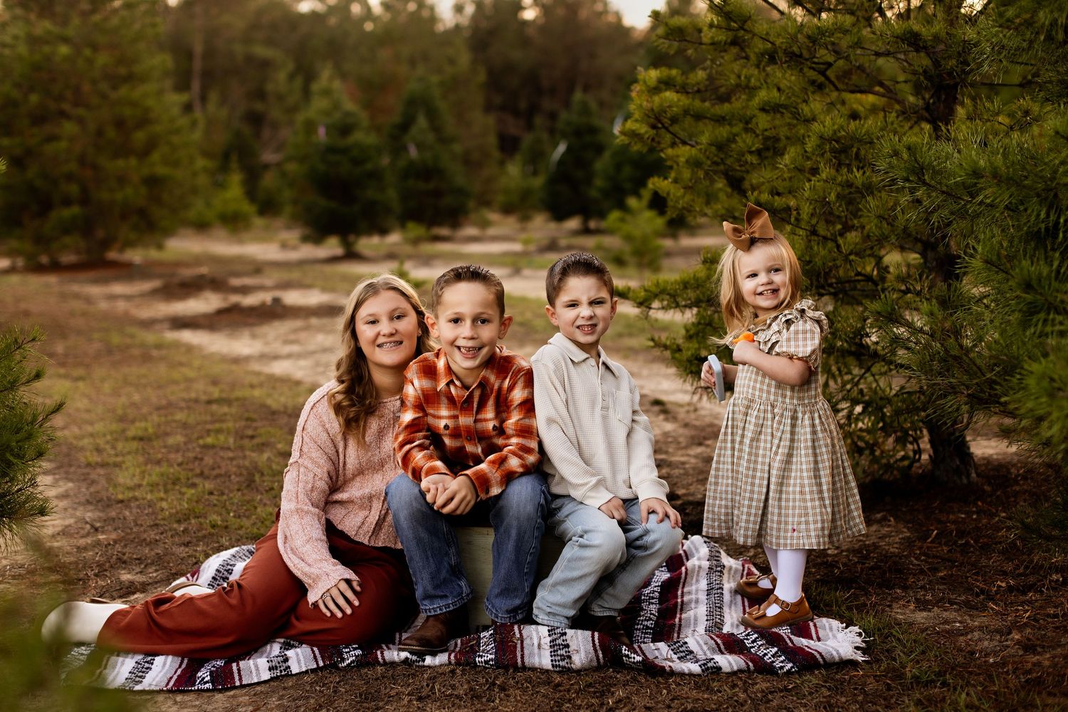 A family sits together on a picnic blanket among evergreen trees during a holiday photo session.
