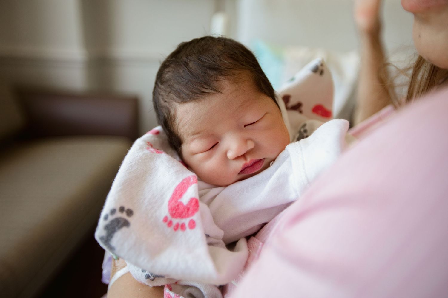 Sleeping newborn wrapped in footprint-patterned blanket resting against pink clothing.