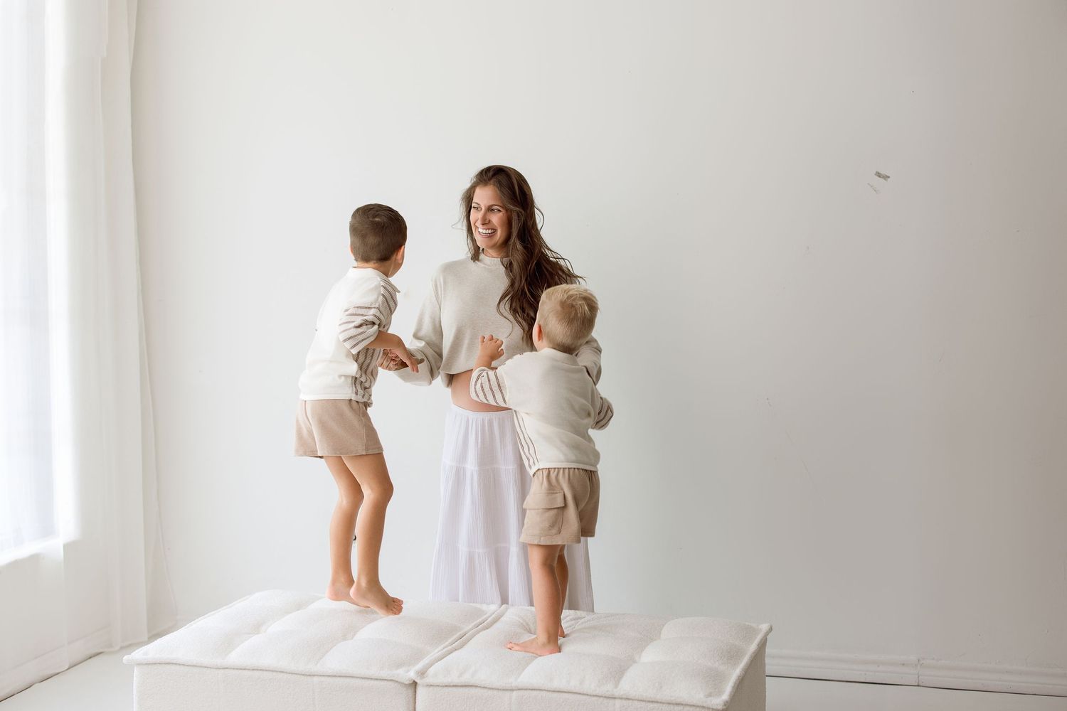 A parent and baby interact playfully in a bright, minimalist white room with natural light streaming through windows.
