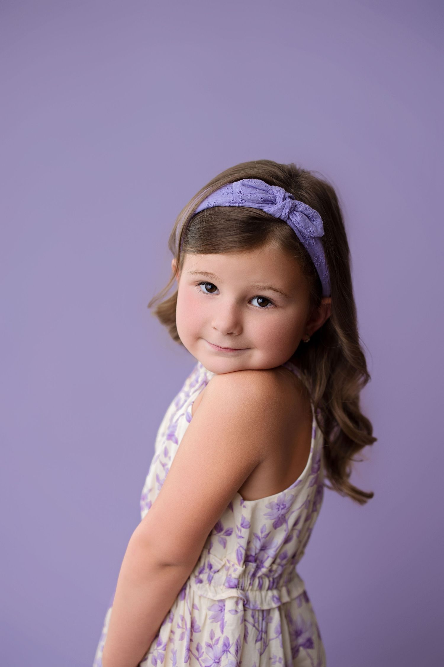 A young child in a floral dress with purple headband poses against a lavender background in a multi-angle portrait series.