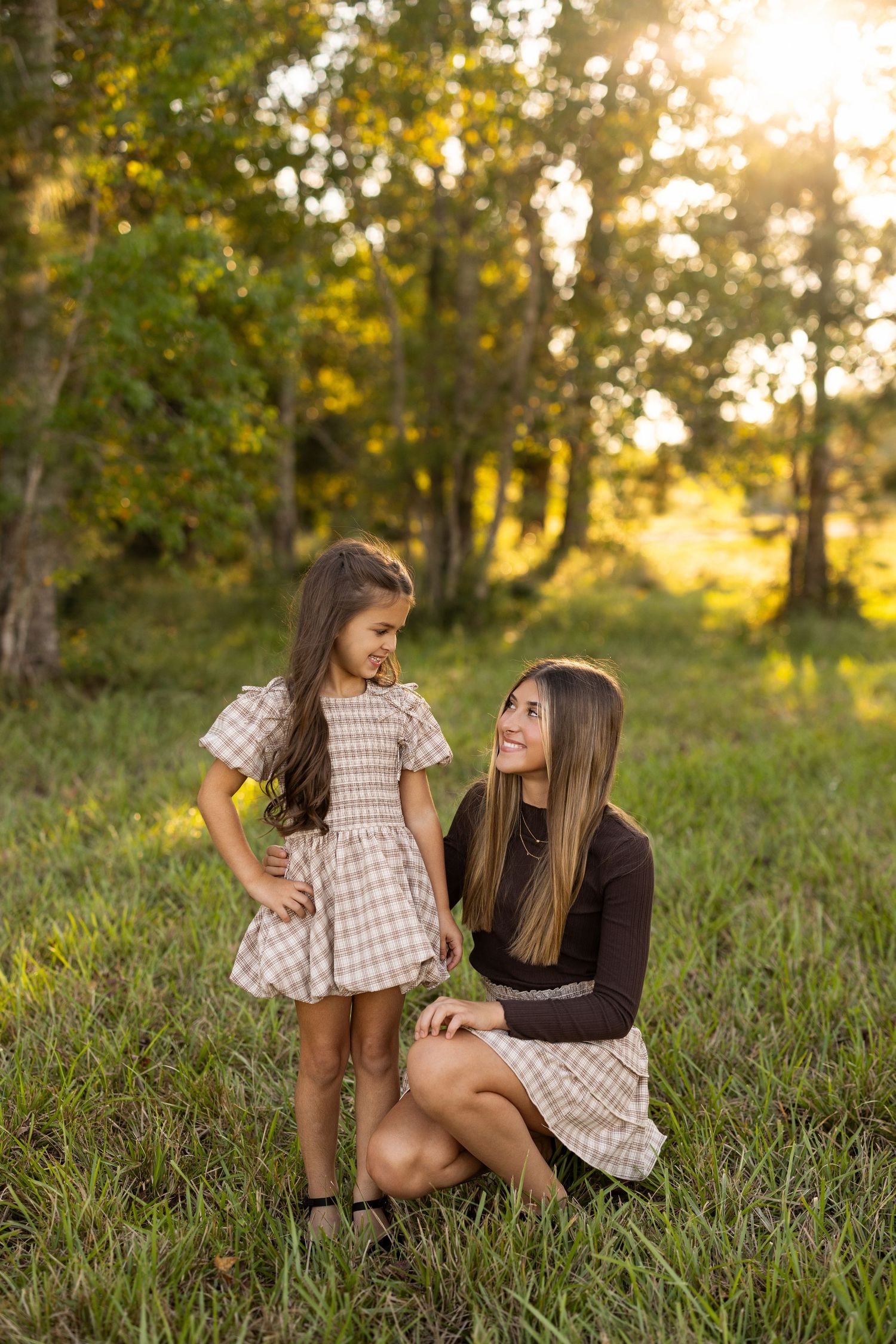 Two people sit together on grassy ground during golden hour in a natural outdoor setting.