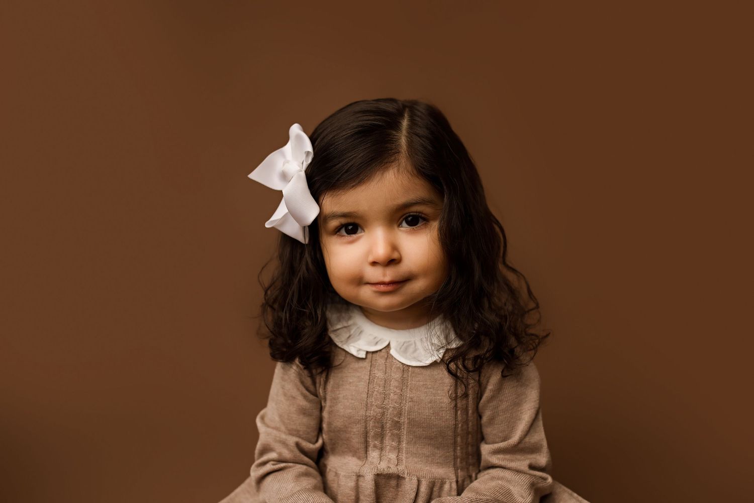 Child in vintage-inspired outfit during classic portrait session against brown background.