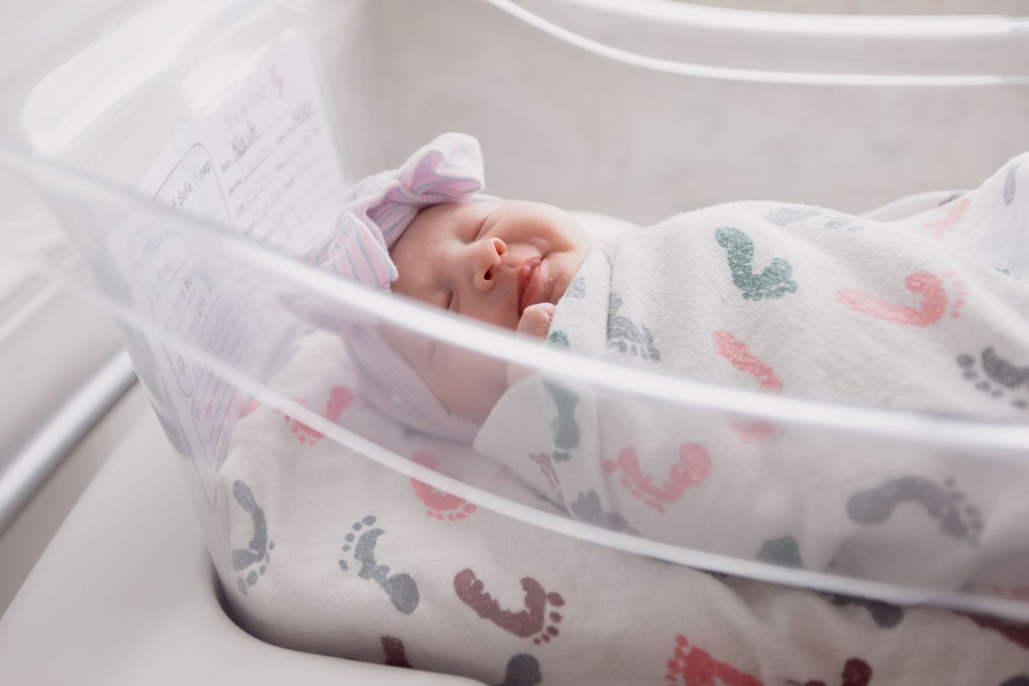 Baby swaddled in white blanket with pink and gray butterfly pattern sleeps peacefully in crib.