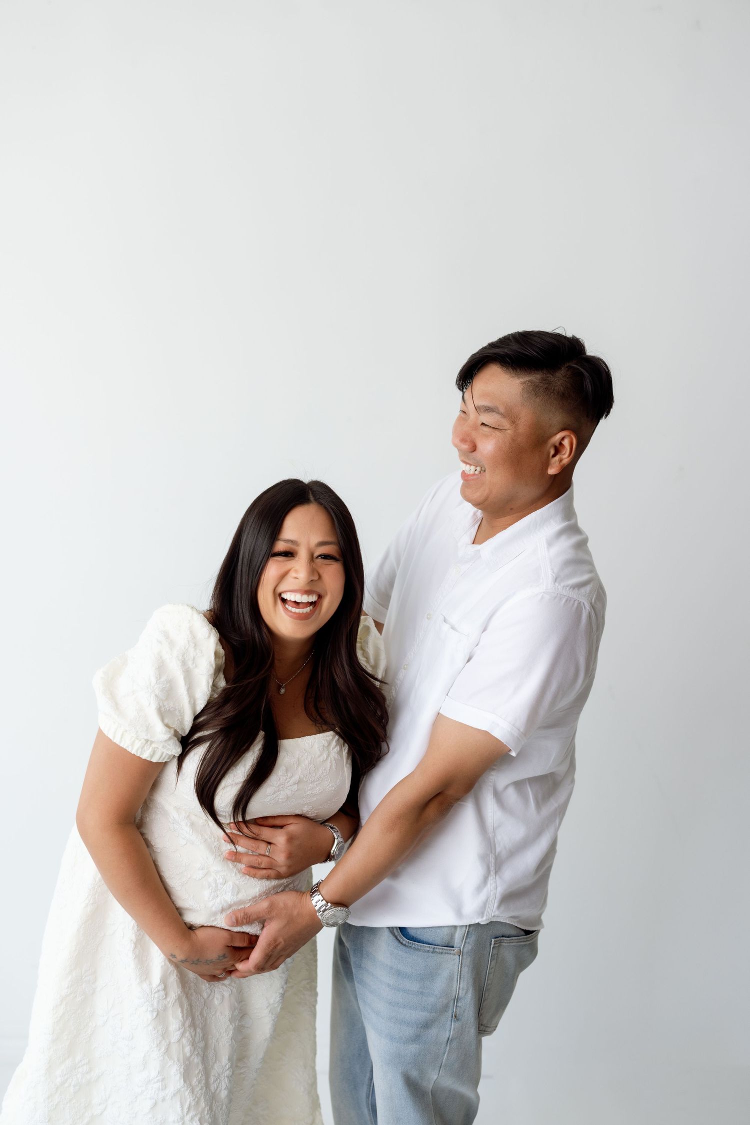 A couple in white outfits share playful and intimate poses against a light background in a triptych series.