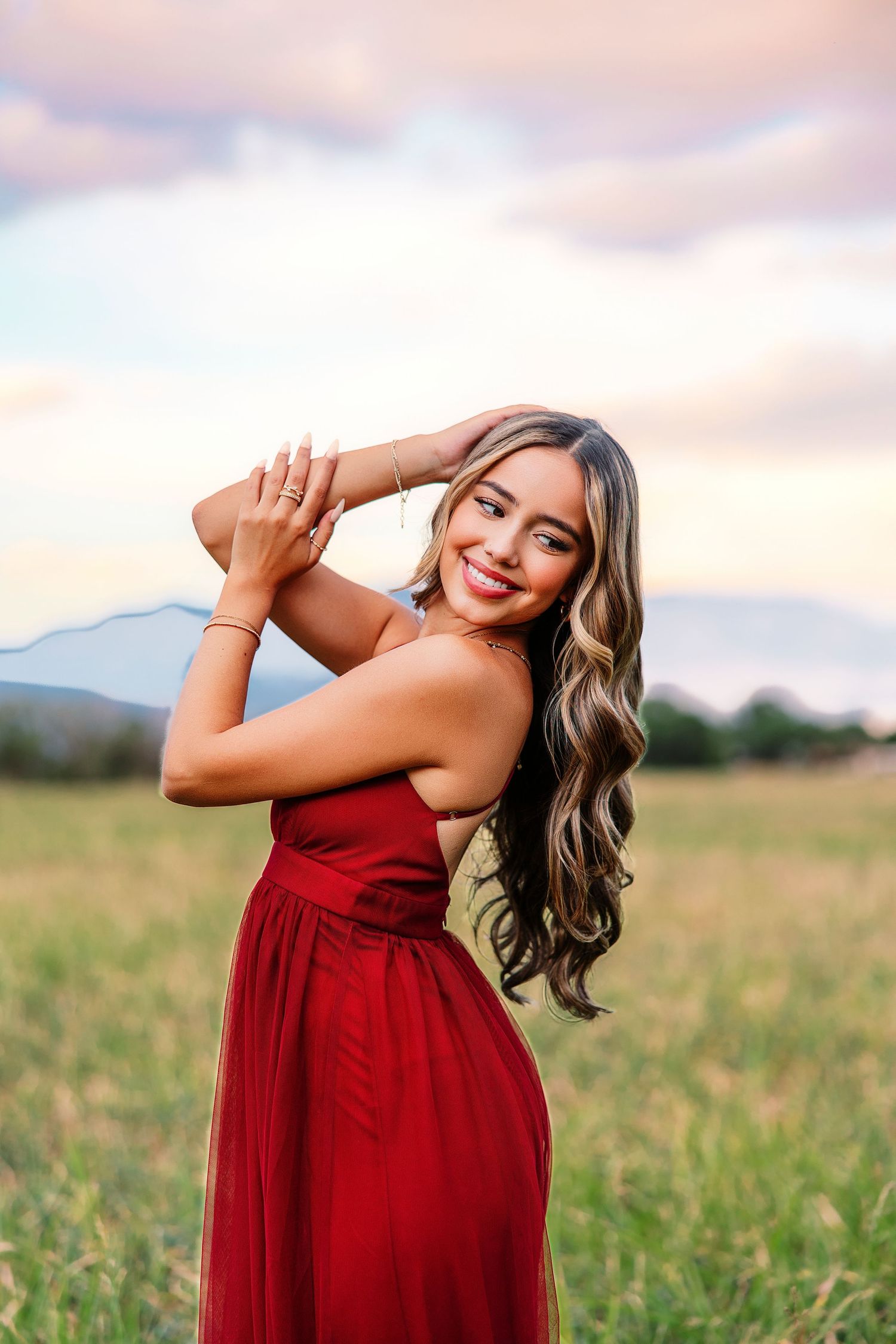 Person in red dress poses playfully in field during golden hour sunset photoshoot.