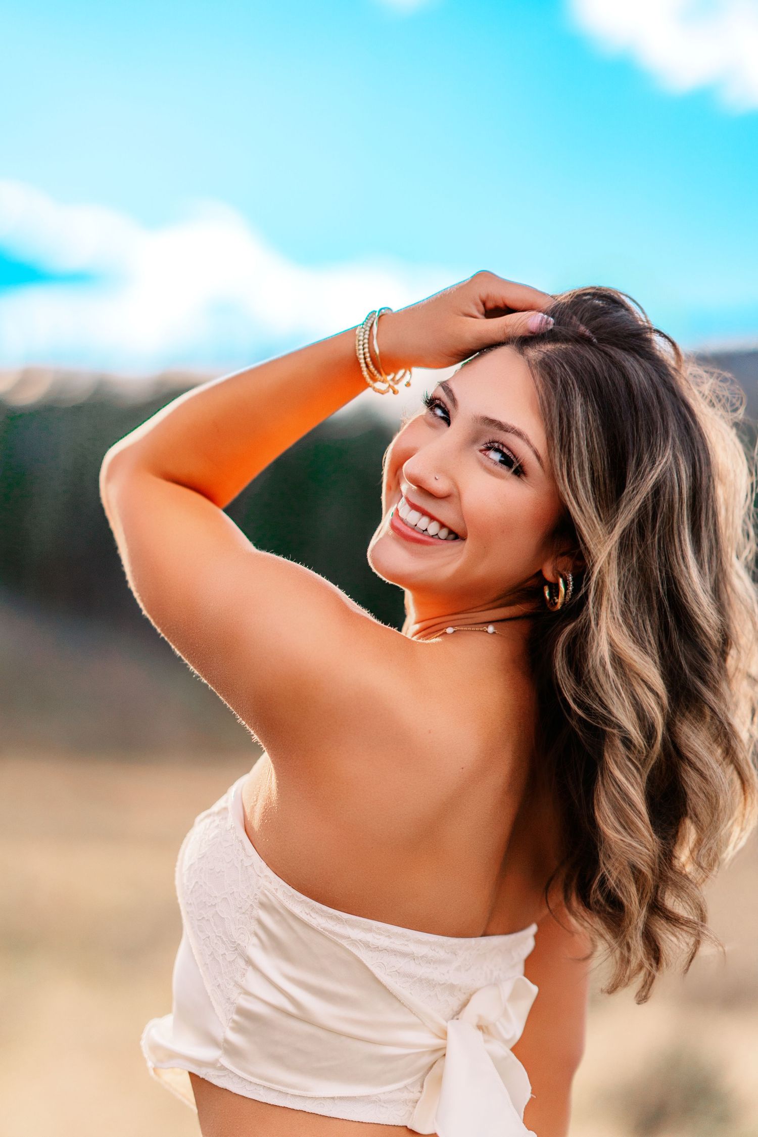 A portrait of someone in casual attire against a bright blue sky with mountains in the background.