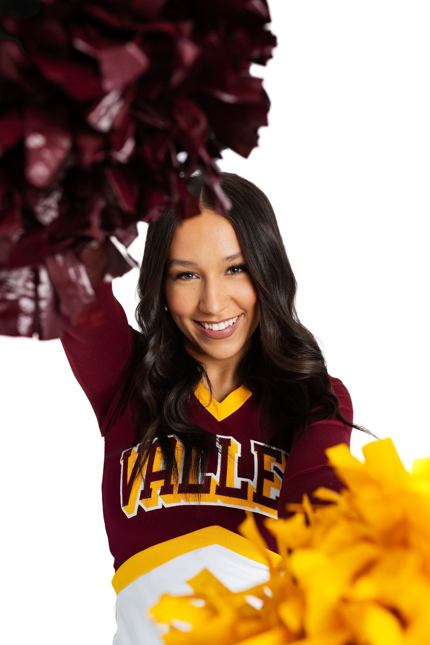 Spirited sports portrait with maroon and yellow uniform and pom poms against white background.