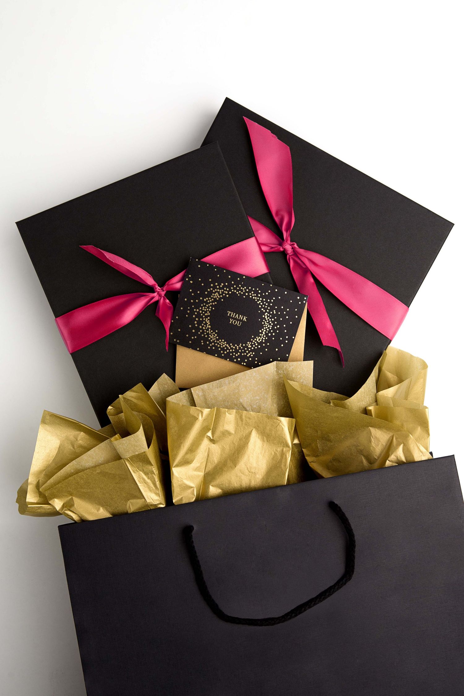 Black gift boxes with pink ribbons and gold tissue paper arranged in a retail display.