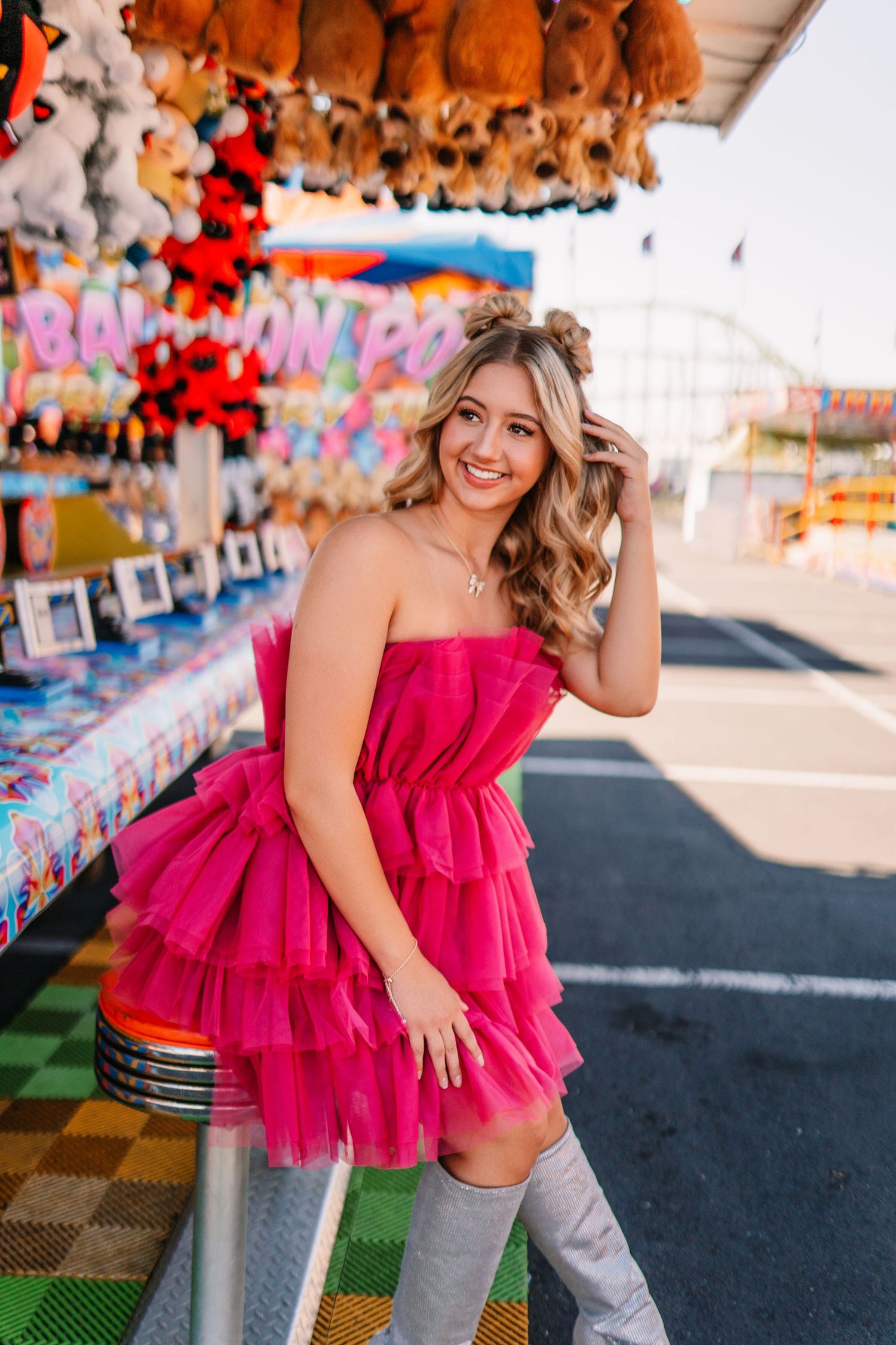 Pink tulle dress photoshoot at a carnival with colorful game booths in background.