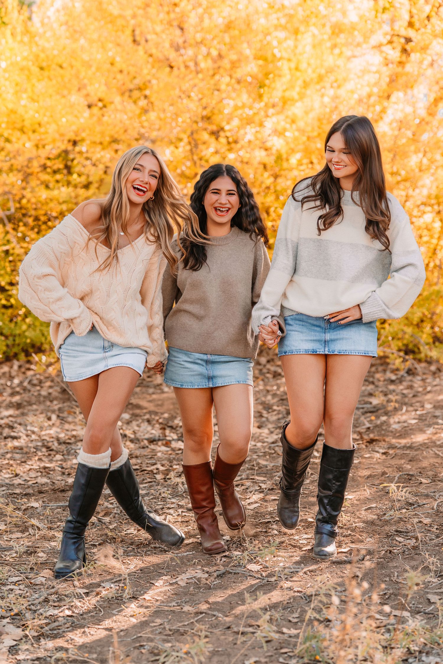Friends wearing cozy sweaters and boots posing together on autumn leaves.