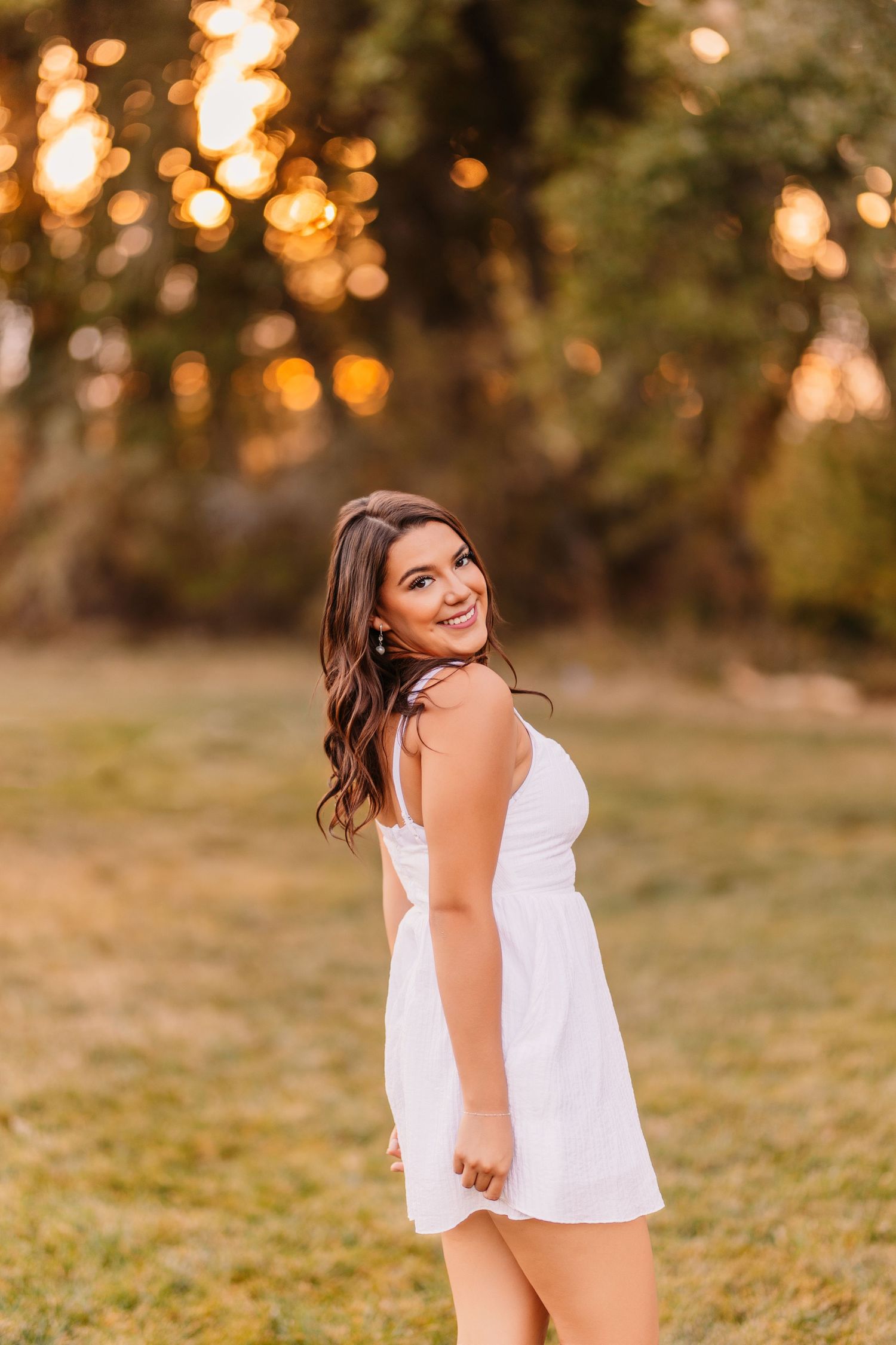 Golden hour portrait session in a grassy field with warm bokeh lighting effects.