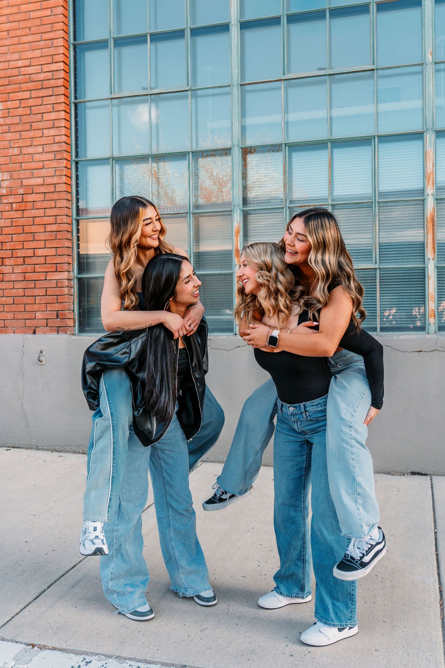 Friends in matching denim and black jackets pose playfully against industrial building backdrop.