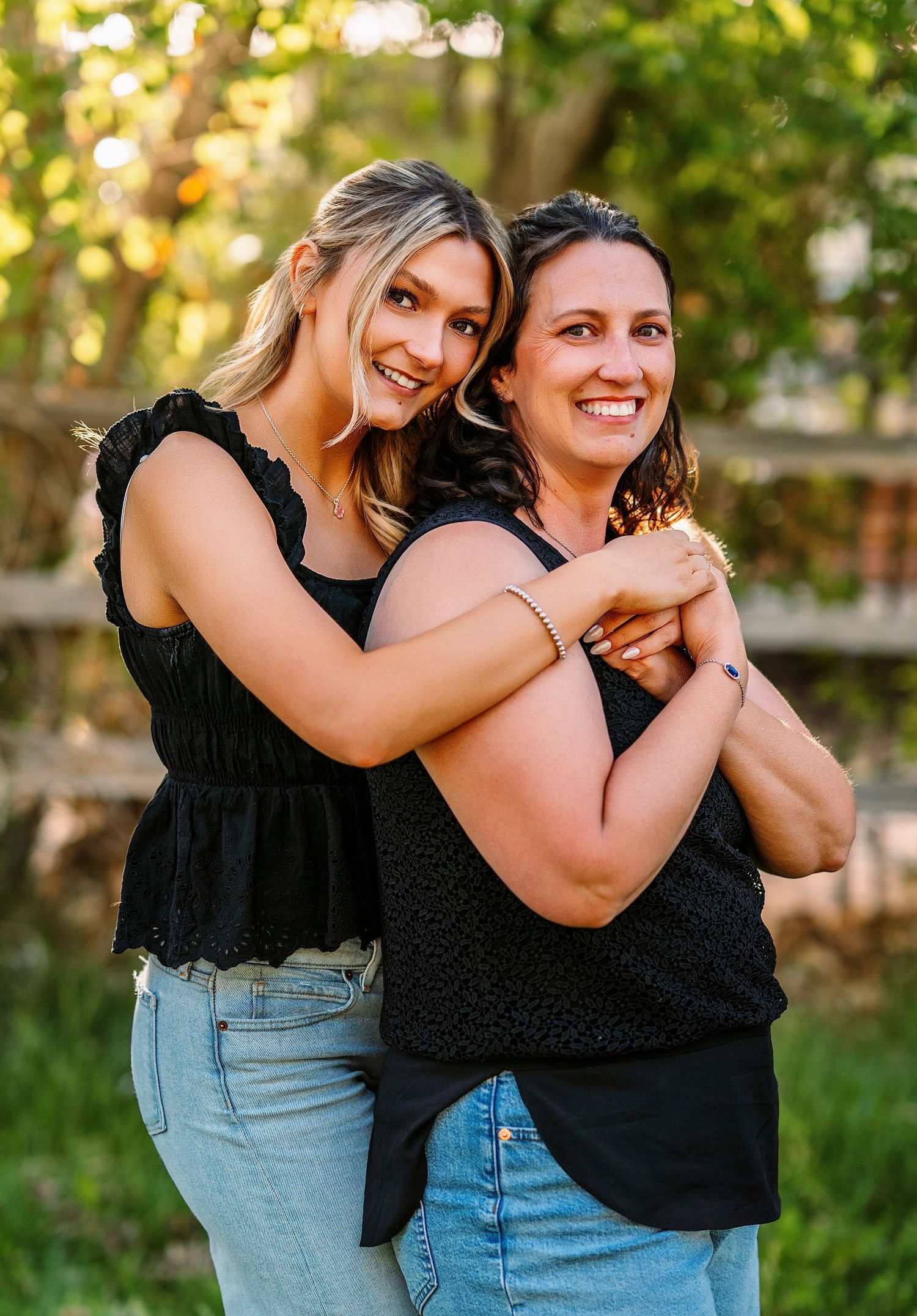 Two friends in casual outfits share joyful embrace outdoors during golden hour.
