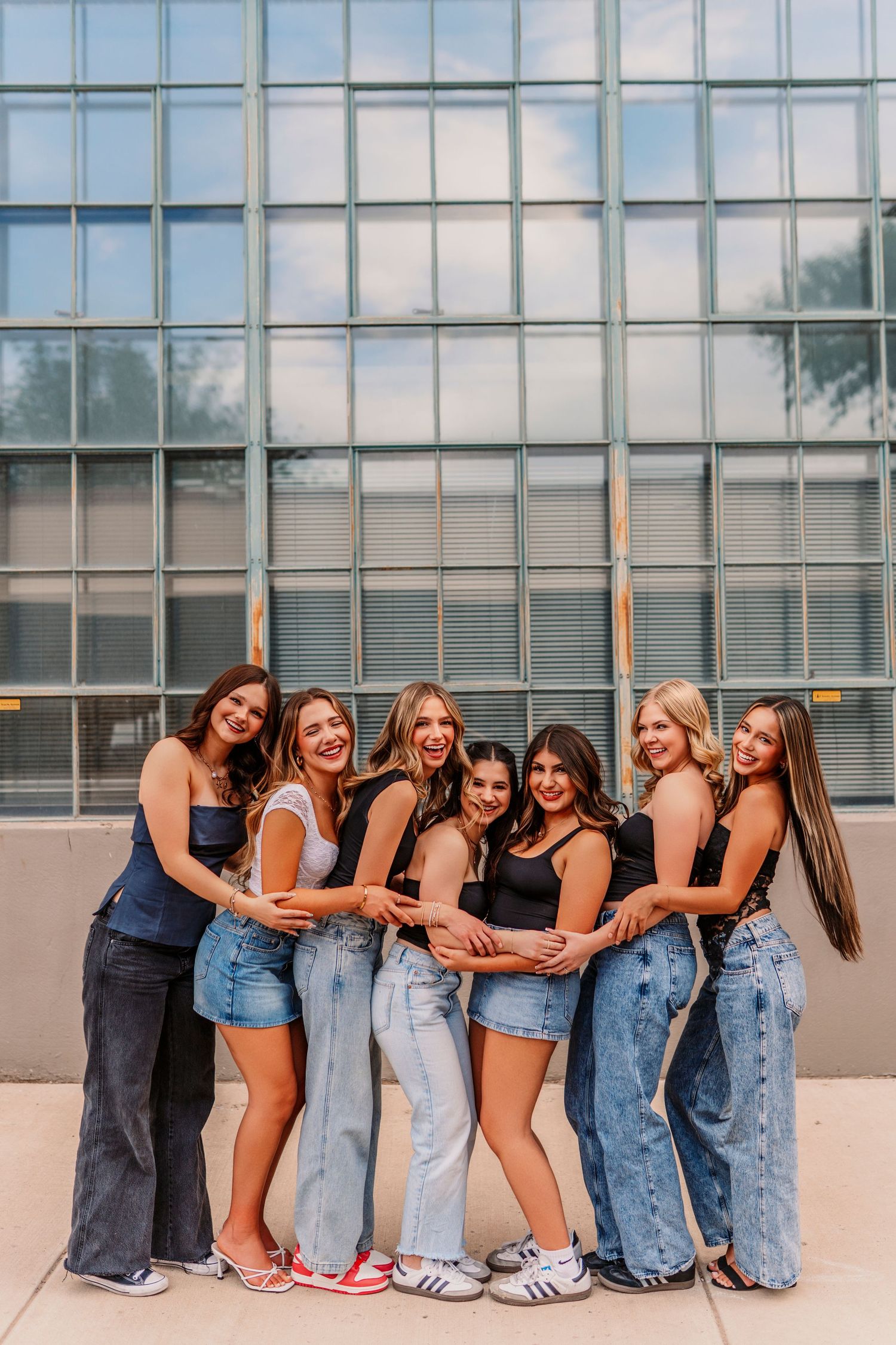 Friends in denim posing together against modern glass building exterior.