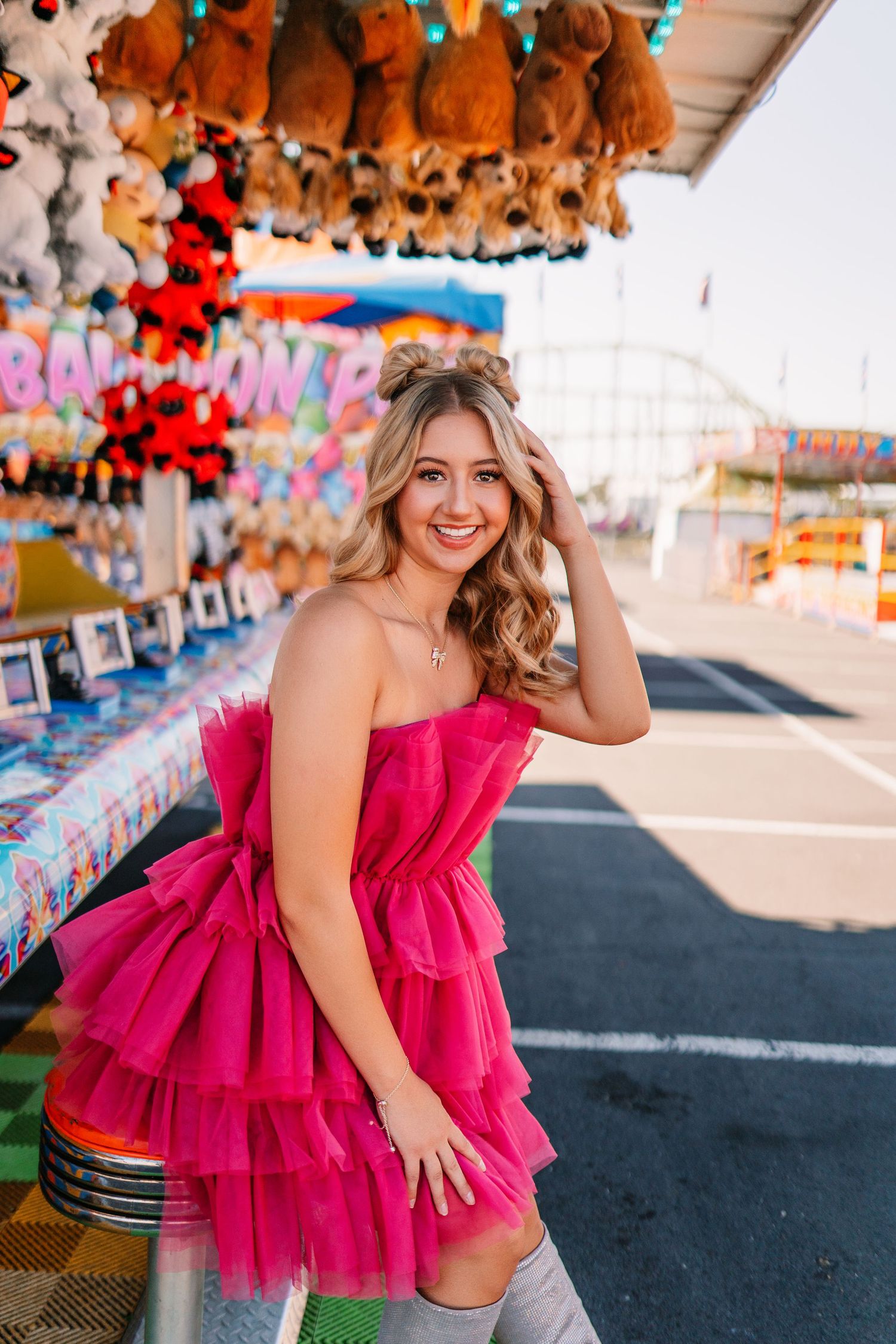 Vibrant carnival scene with hot pink ruffle dress against backdrop of plush prizes and game booths.