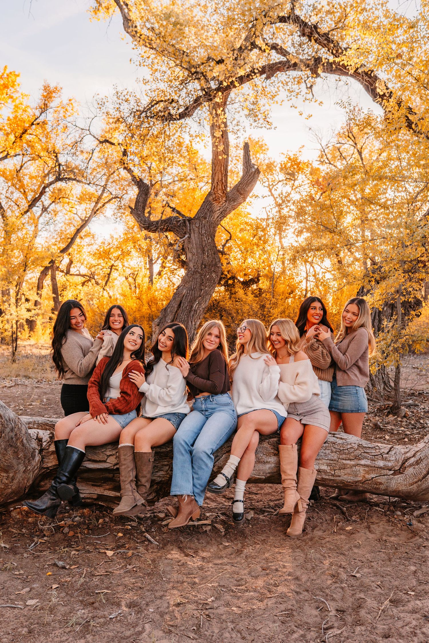 Group sitting casually on fallen logs with autumn trees glowing golden in the background.
