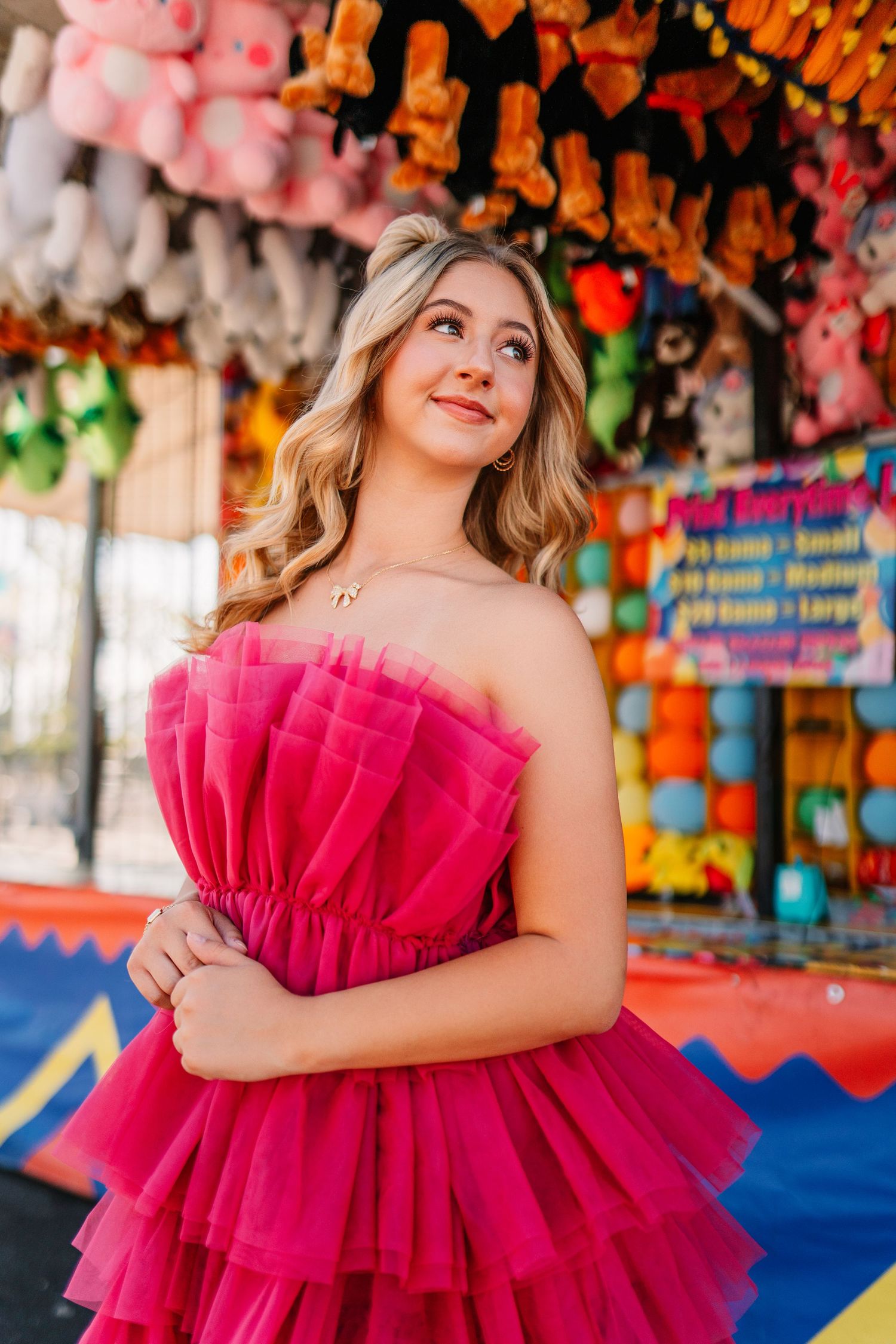 Vibrant carnival scene with pink tulle dress against colorful stuffed animal prizes and carnival game backdrop.