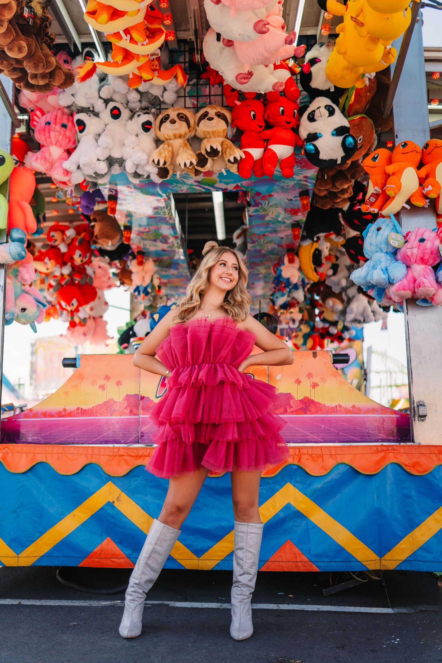 A bright pink tulle dress stands out against colorful carnival game booths with stuffed animal prizes.