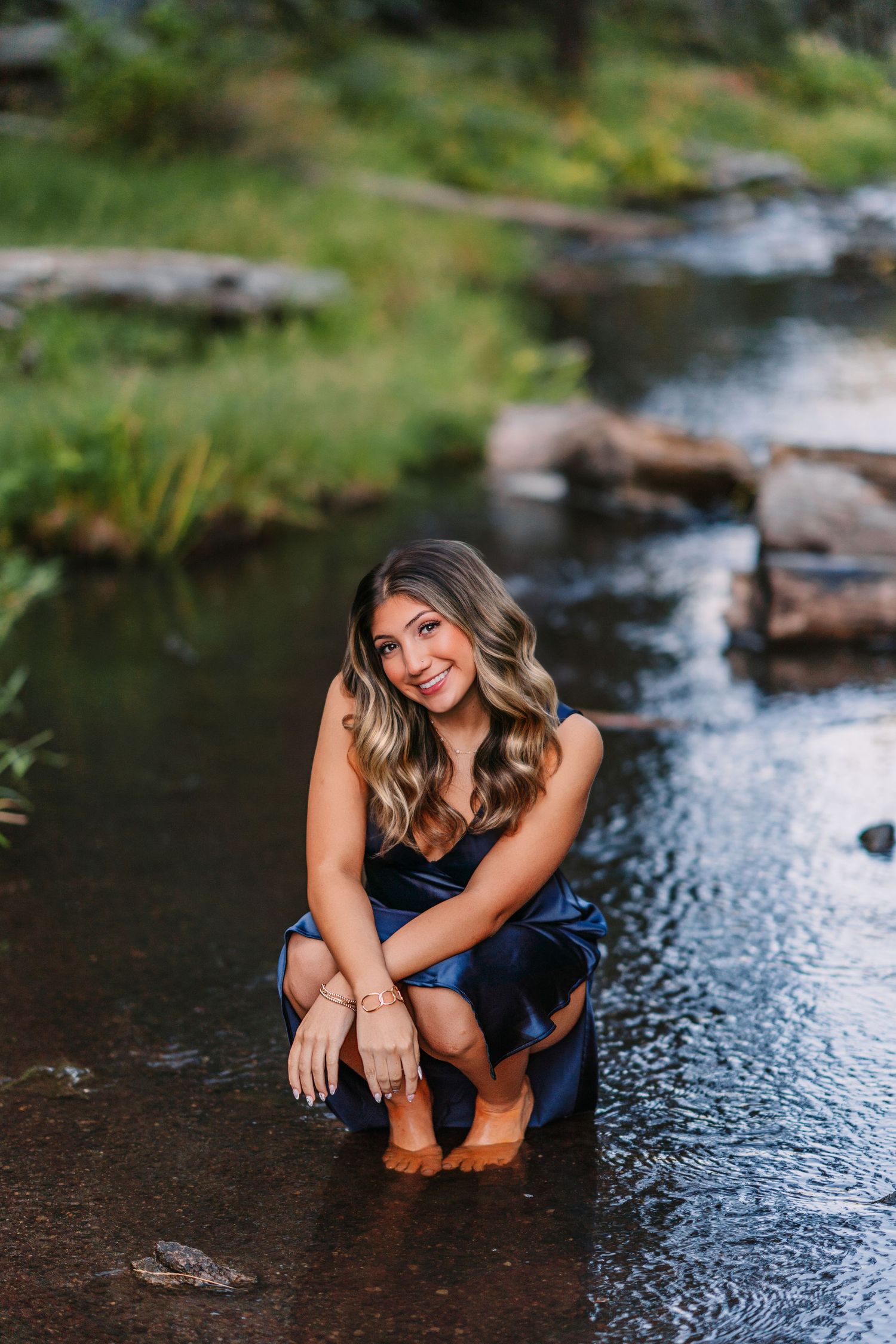 A casual outdoor portrait by a stream with someone sitting on wet rocks in nature.