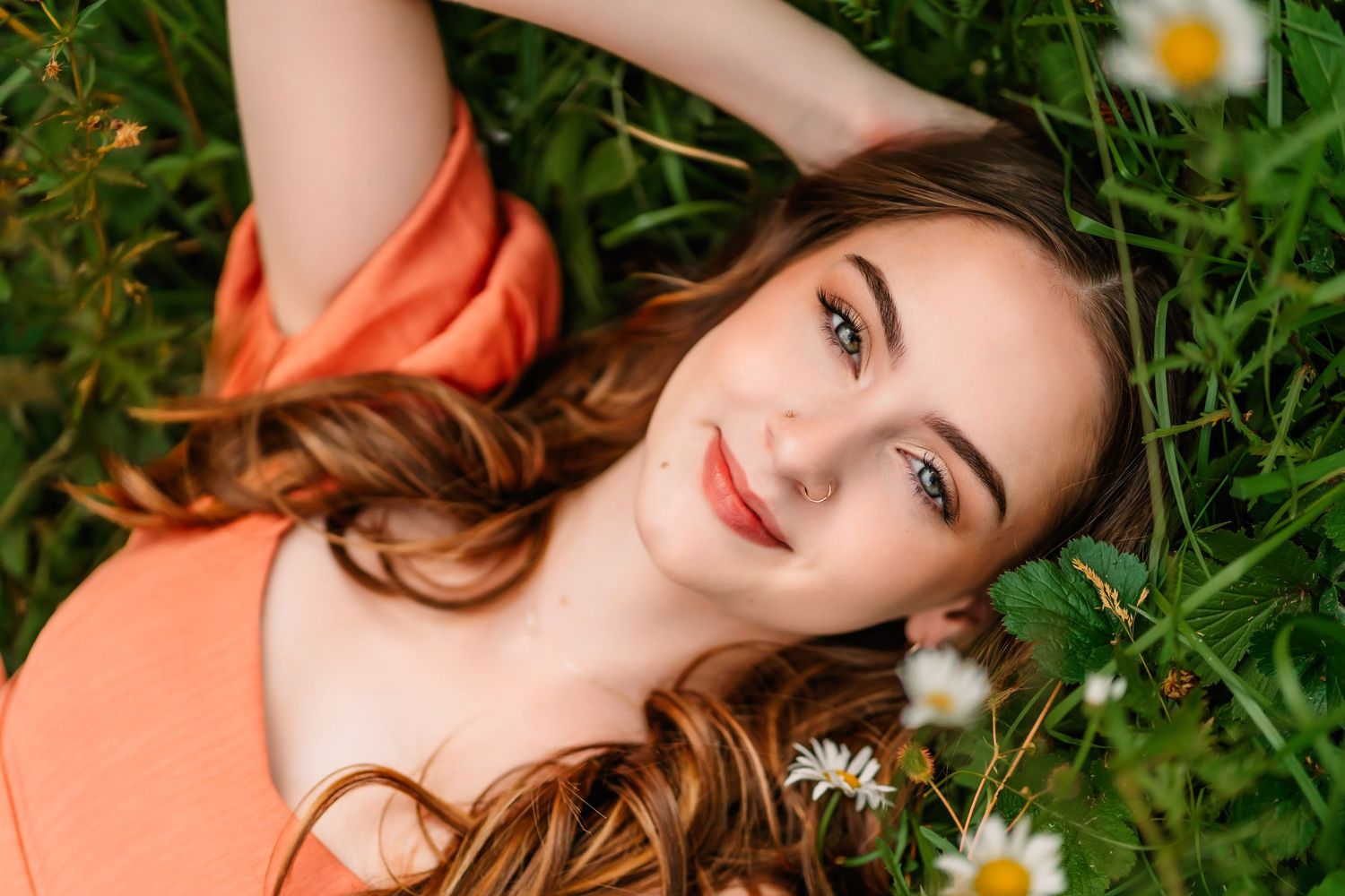 Artistic portrait in coral dress laying among wildflowers and daisies.
