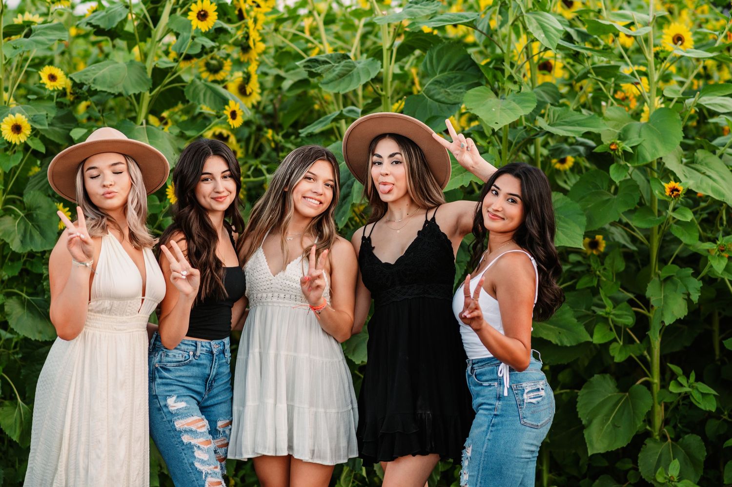 Group wearing casual summer outfits poses together in front of blooming sunflowers and greenery.