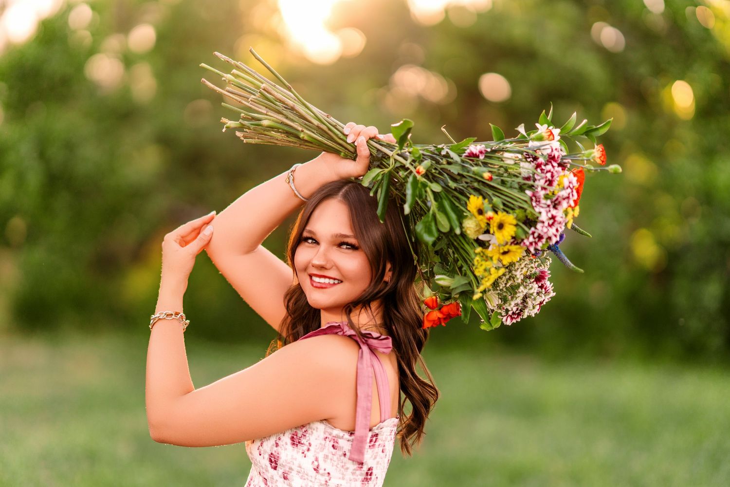 A person in a pink dress poses with wildflowers in a golden sunlit field during sunset.