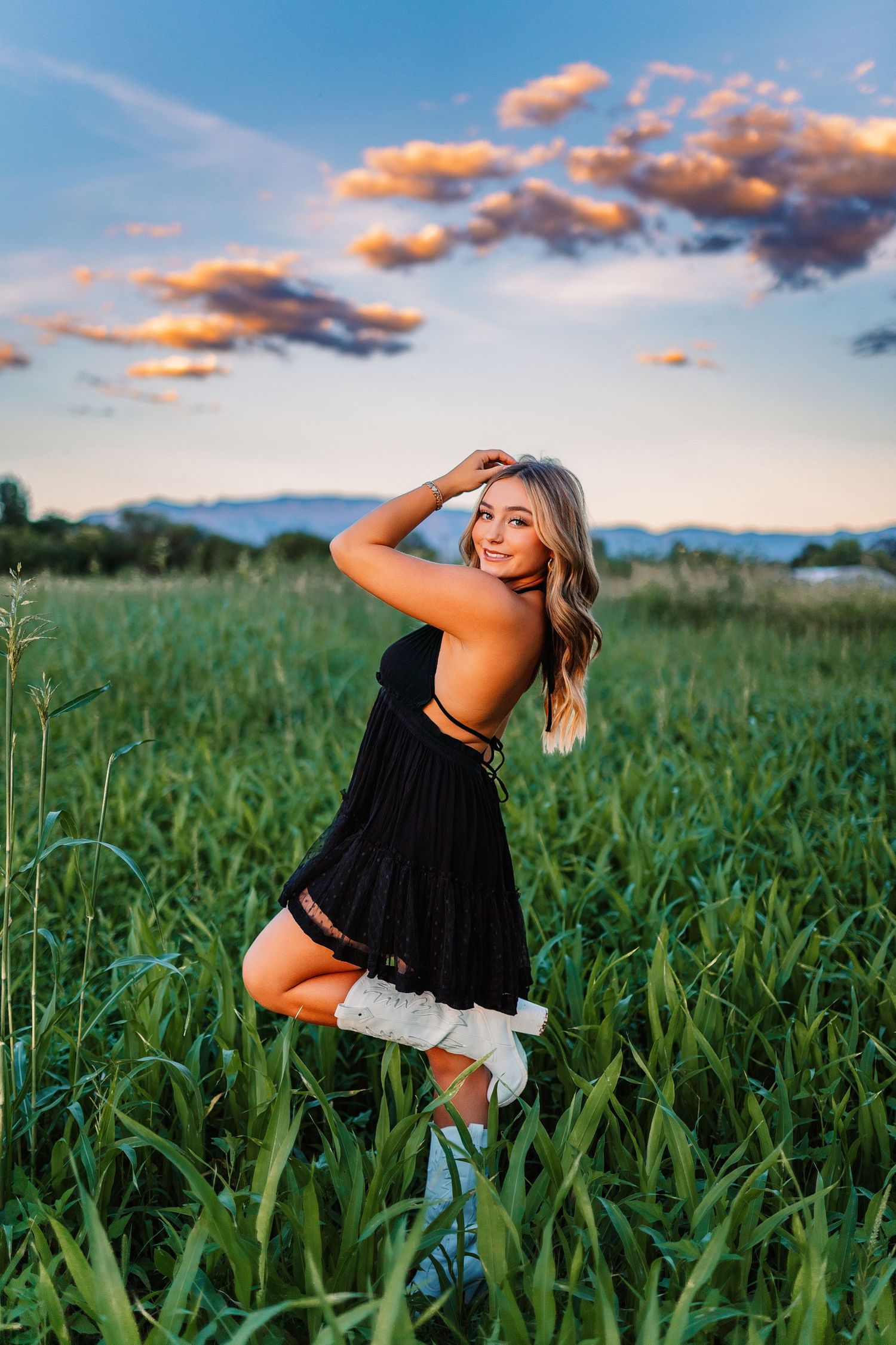 Outdoor photoshoot in a green field with dramatic sunset sky and casual summer attire.