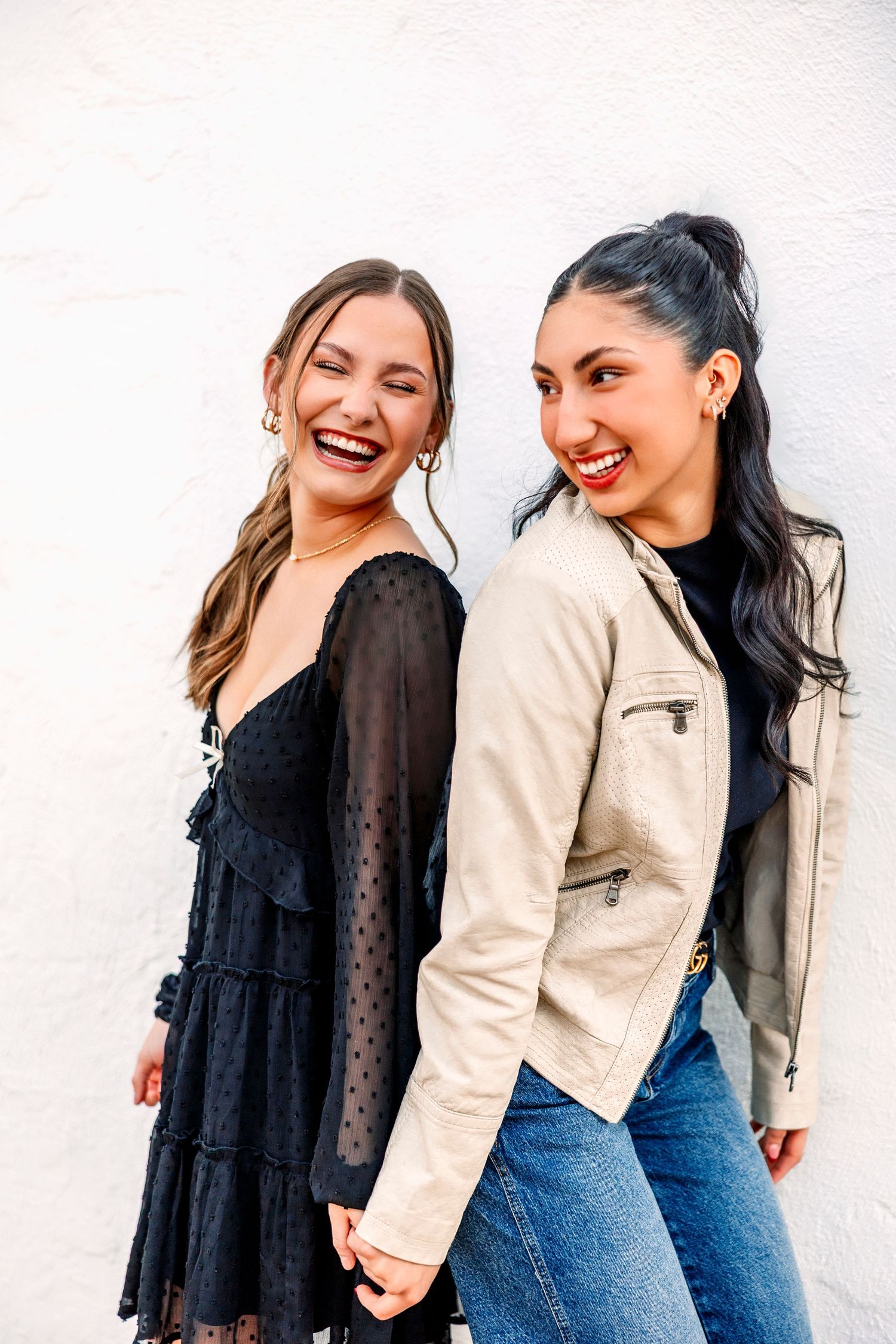 Two people share genuine laughter while posing against a white wall in casual outfits.
