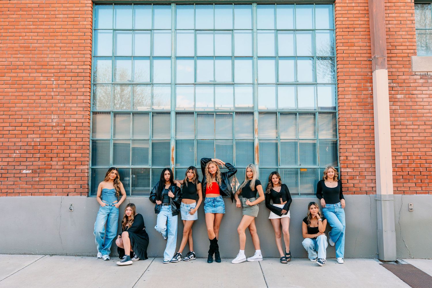 A group poses casually against a brick wall with large windows, creating a relaxed urban vibe.