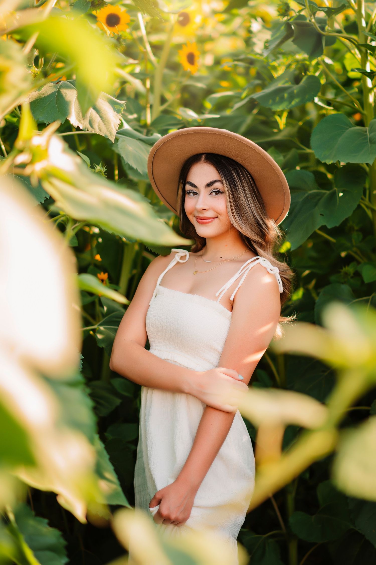 Portrait session in a sunflower garden wearing a white dress and brown hat.