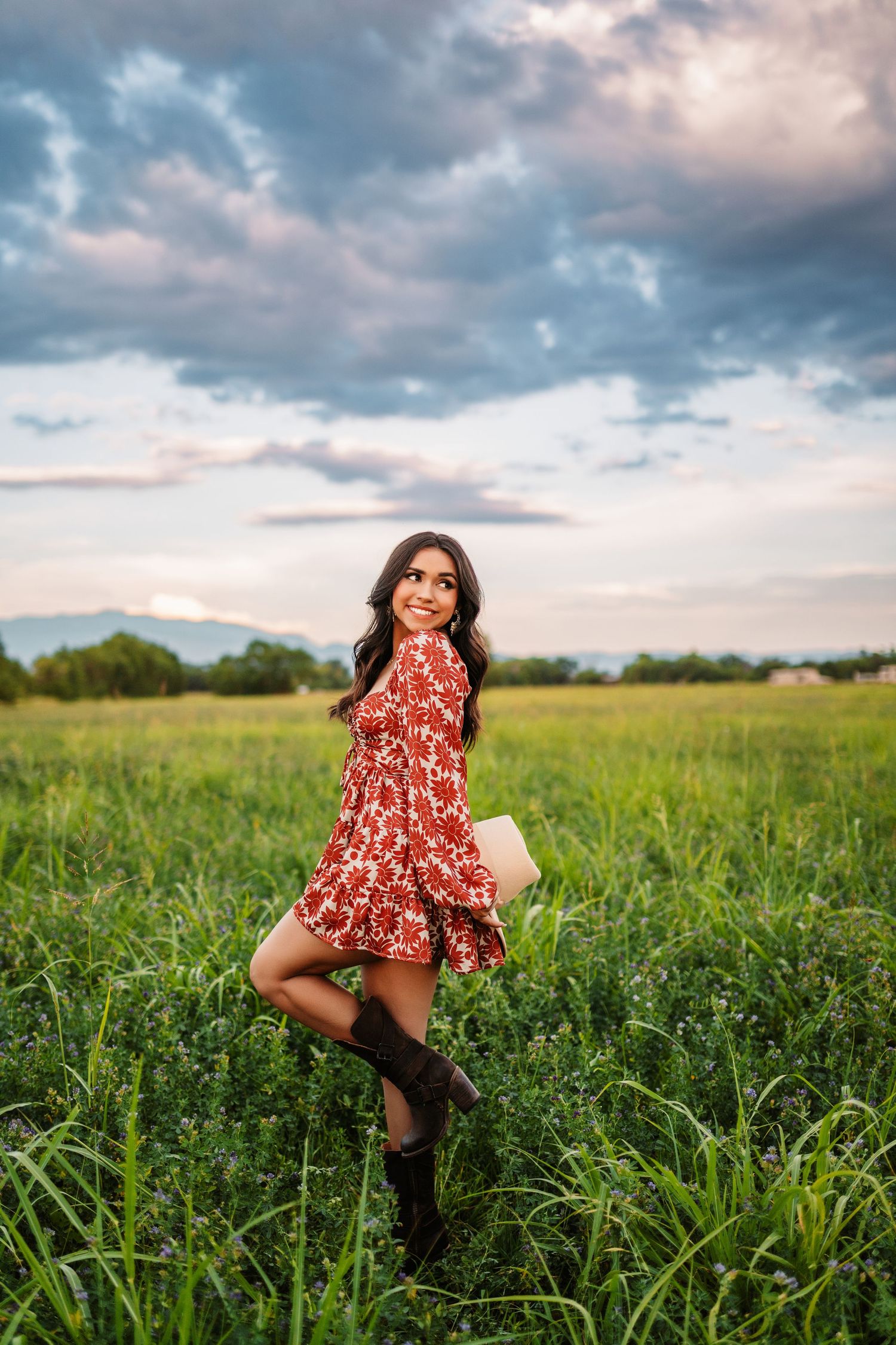 Person in red floral dress twirling and dancing in a green field at sunset.